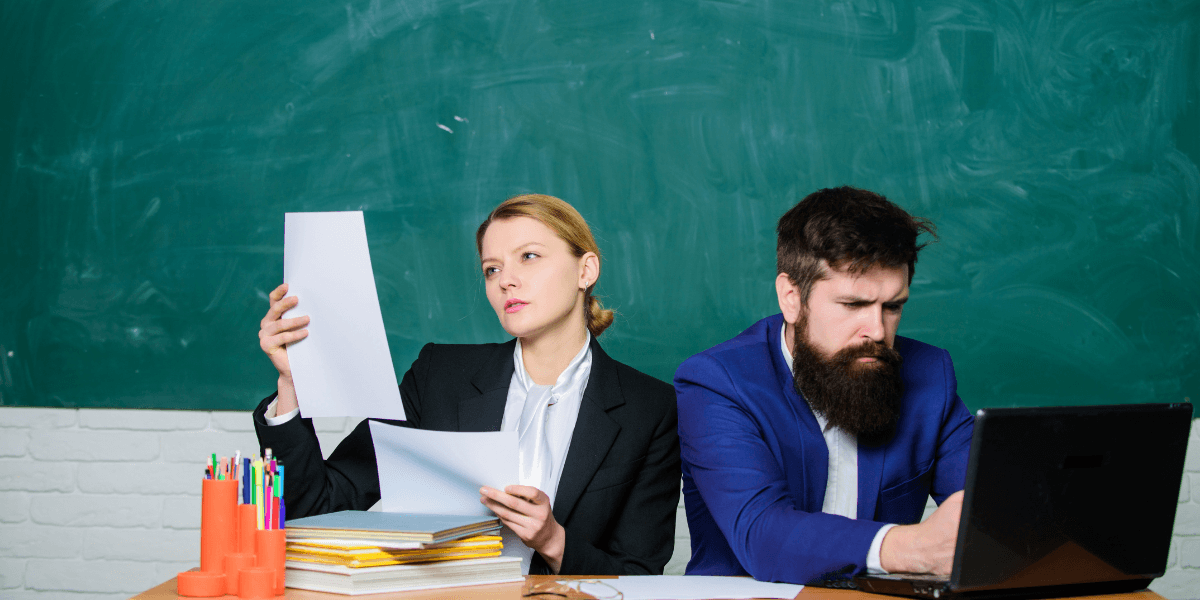 Two professionals in business attire seated at a desk, reviewing documents and discussing work-related matters.