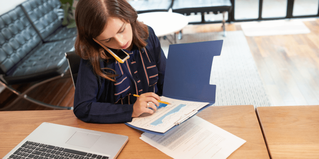 A woman focused on her laptop, seated at a desk with a notepad and pen nearby.