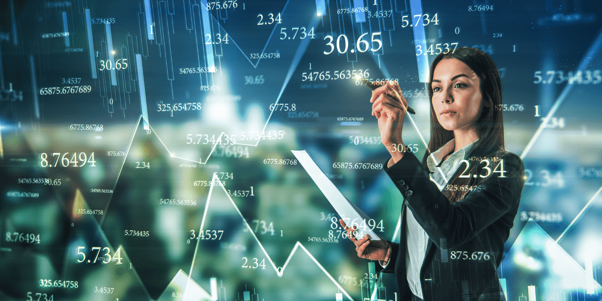 A businesswoman in a suit points at a screen displaying graphs and numbers, indicating data analysis or presentation.