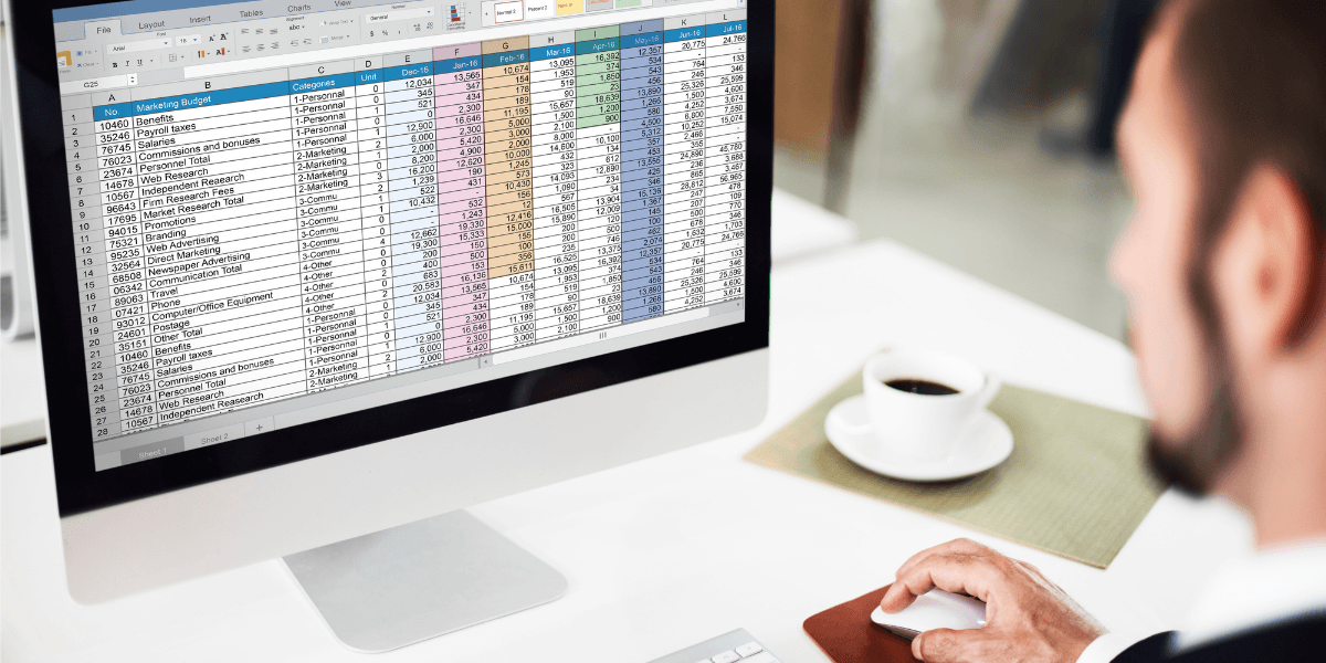 A man focused on a computer screen, working on an Excel spreadsheet with data and charts displayed.