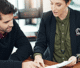 A man and woman sit at a table, reviewing documents and discussing their contents.