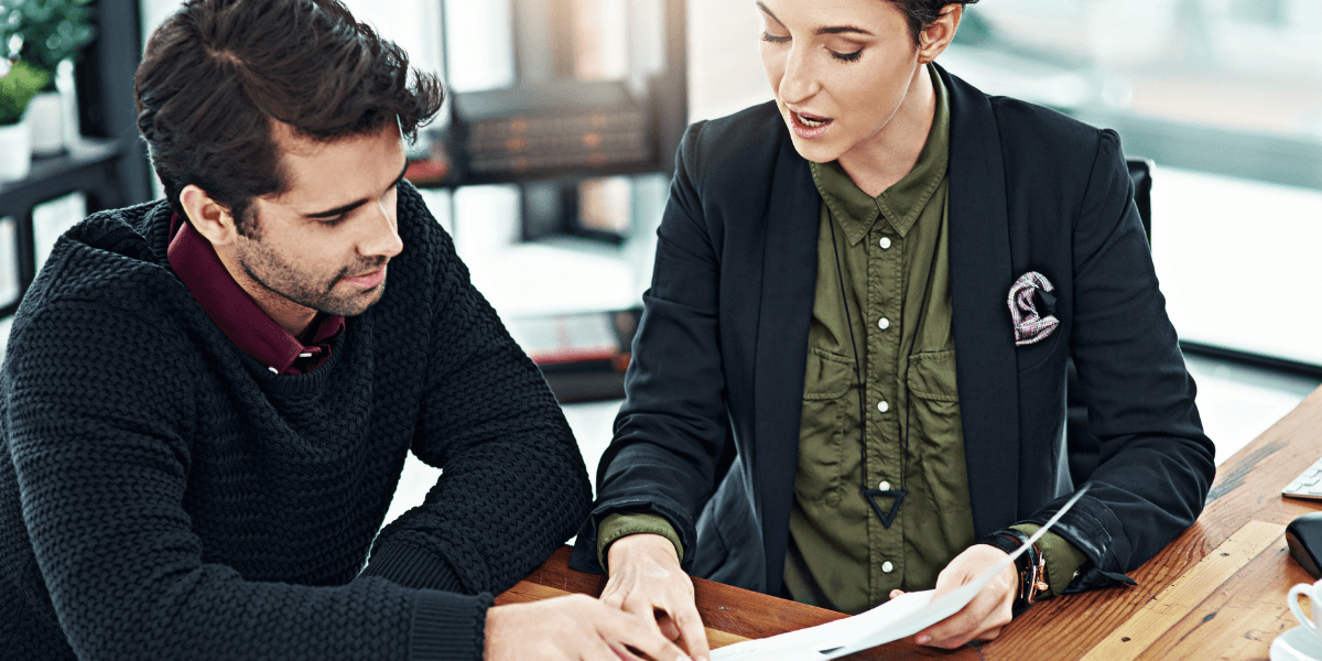 A man and woman sit at a table, reviewing documents and discussing their contents.