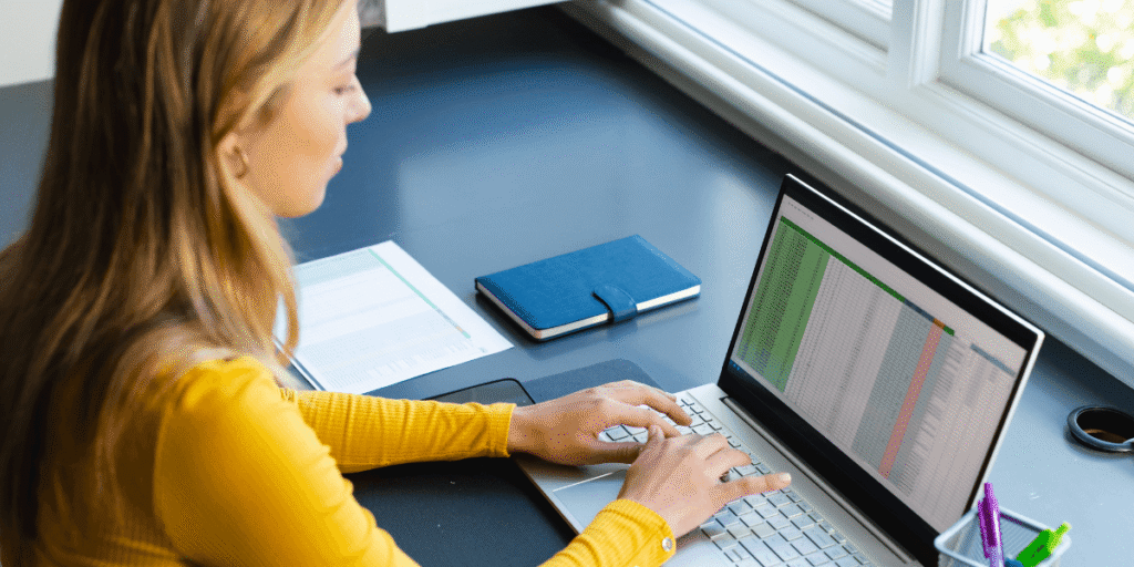 A woman focused on her laptop, typing intently in a well-lit workspace.