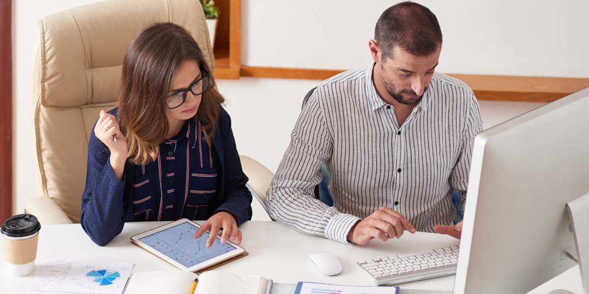 A man and woman collaborate on a computer, focused on their work in a modern office setting.