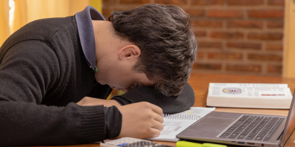 A man is sleeping at his desk, resting his head on his hand, appearing tired and overwhelmed.